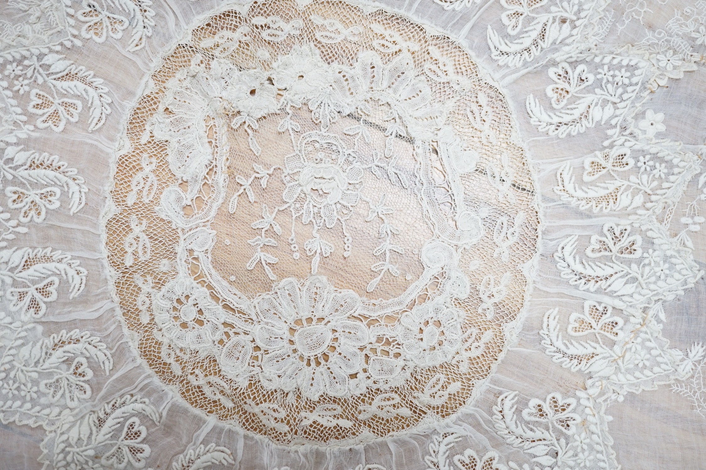 A late 19th century Normandy lace table cover of hand spun linen, hand white worked, with Brussels Point de Gaze insertions and bobbin lace edging, together with two feathers and a net veil